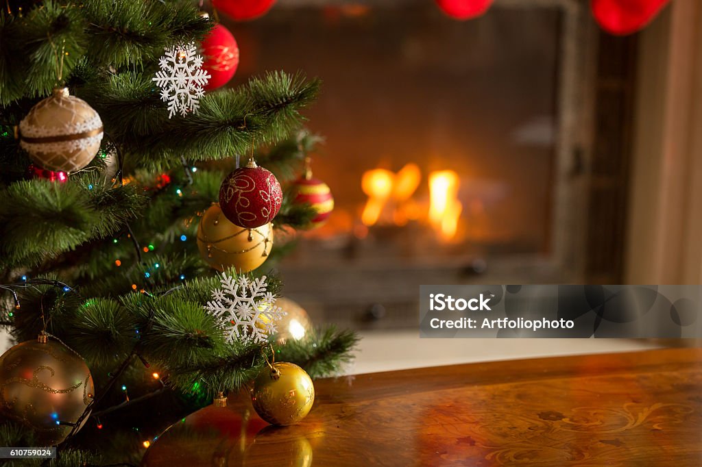 Closeup image of golden baubles on Christmas tree at fireplace Closeup image of golden and red baubles on Christmas tree in front of burning fireplace. Beautiful Christmas background Christmas Stock Photo