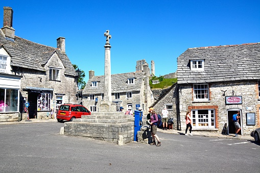 Corfe, United Kingdom - July 19, 2016: Stone cross in the village centre with the castle to the rear, Corfe, Dorset, England, UK, Western Europe.