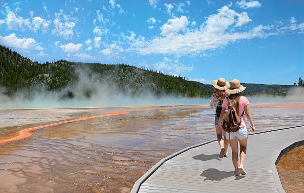 Girls hiking on vacation in beautiful park. Girls wearing hats hiking on vacation. Beautiful Grand Prismatic Spring at Yellowstone National Park. midway geyser basin photos stock pictures, royalty-free photos & images