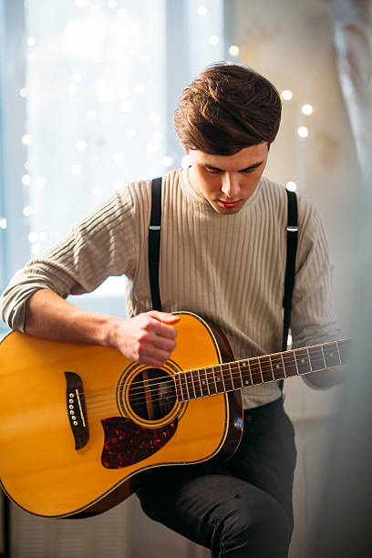 istock Young man sitting at home and playing guitar dramatic 610768446