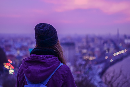 Traveler hipster looking at winter evening cityscape and purple sky