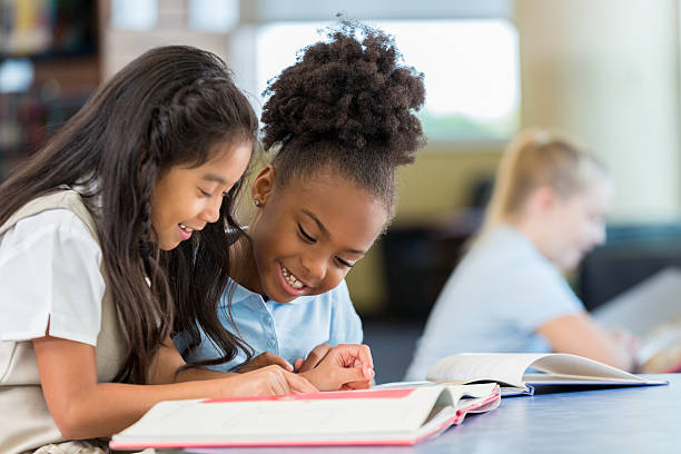 des écolières souriantes et gaies lisant un livre ensemble à l’école - schoolgirl photos et images de collection