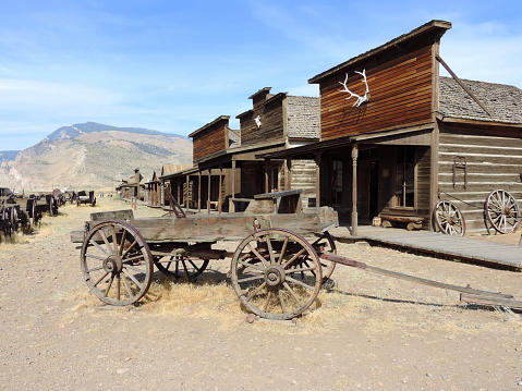 Old western style horse drawn wagons lined up in front of old western buildings,\n\nTaken in Cody, Wyoming, USA.