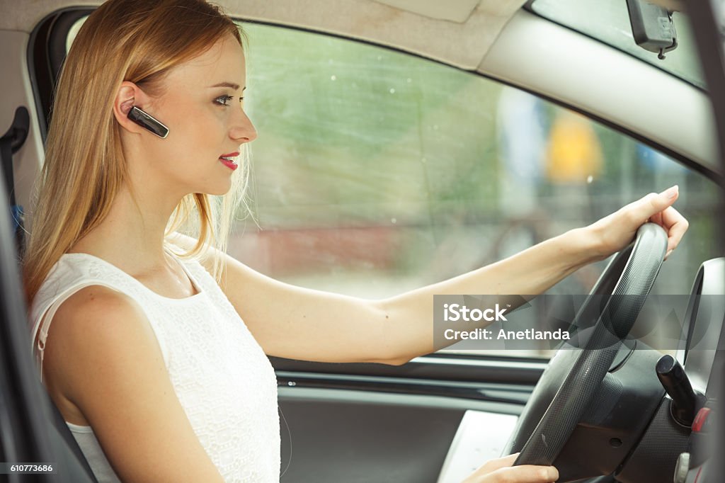 woman driving car with headset Transport and safety concept. Young blonde woman driving car using her mobile phone and headset, side view Bluetooth Stock Photo