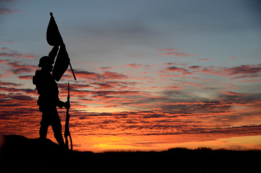 Soldier silhouette carrying a flag across a field at sunset.  The silhouette was made from a memorial located in a vacated church property near Summerside, Prince Edward Island. No copyright was evident.