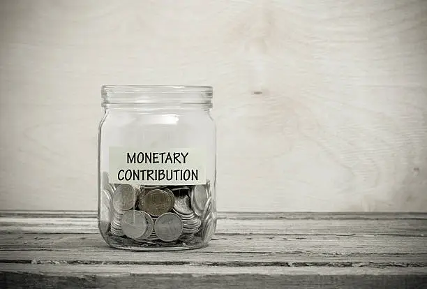 Label on a glass jar with the inscription - monetary contribution. Glass jar with coins. Financial concept on wooden background
