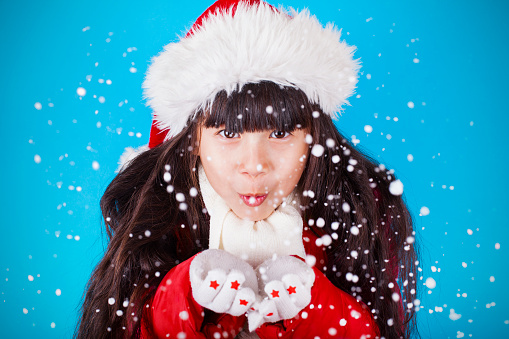 Asian little girl in Santa Claus hat blowing snowflakes