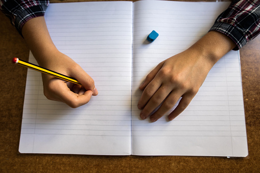 Close up of a child writing with pencil into empty workbook.
