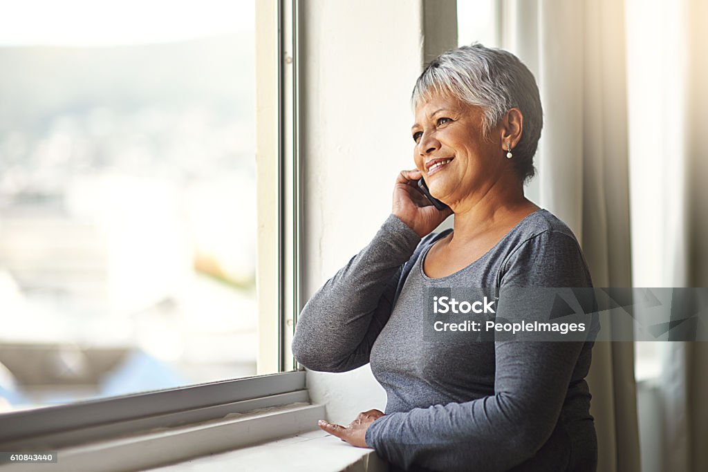 One hello can make someone’s day Shot of a mature woman using her cellphone at home Using Phone Stock Photo