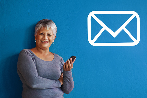 Shot of a mature woman holding a mobile phone with a message icon beside her on the wall