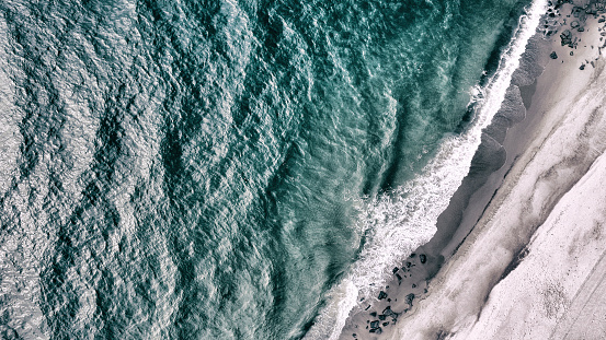 The sea with waves and ripples and the shore with rocks. This image was photographed from above with a drone.