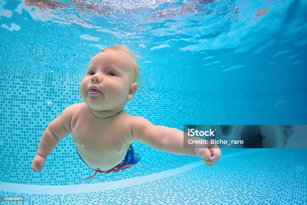 Little baby dive underwater with fun in swimming pool Funny photo of active baby diving in swimming pool with fun, jump deep down underwater. Child learn to swim. Healthy family lifestyle, summer children water sports activity and lessons with parents. Baby - Human Age Stock Photo