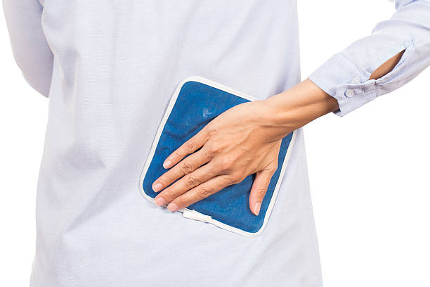 business woman putting an ice pack on her back pain - ice pack fotos imagens e fotografias de stock