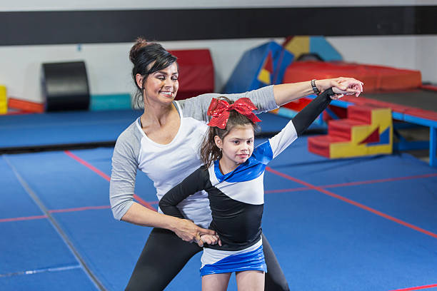 Coach helping autistic girl on cheerleading team A 10 year old girl with autism on a special needs cheerleading squad. She is in a gym wearing her team uniform, working with the coach. cheerleader photos stock pictures, royalty-free photos & images