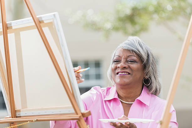 Senior black woman at easel painting on canvas