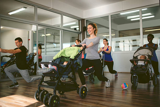Parents Exercising with Their Babies Parents exercising with their babies in the gym. They are working squats and babies are in their strollers. They are happy to exercise together with their babies. Mother and babies looking to fitness instructor. baby squatting stock pictures, royalty-free photos & images