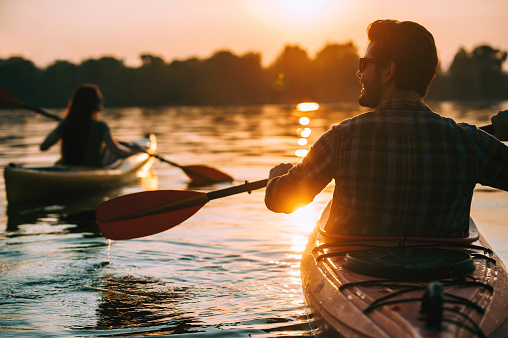 Rear view of young couple kayaking on lake together with sunset in the backgrounds