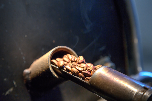 Fresh batch of Arabica coffee beans in the cooling bed of a micro roaster at a small gourmet coffee shop.  Aroma filled smoke and steam are rising from the hot beans