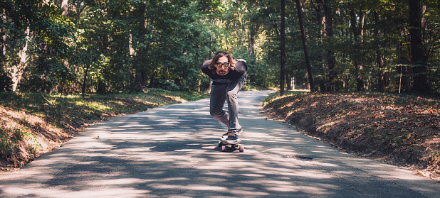 Skateboarder ride a longboard skateboard on the road through the forest. Freeride longboard skating. Panorama view