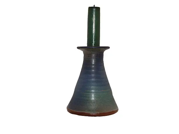 Image of a green candle standing in a blue pottery candleholder isolated on a white background.