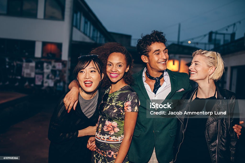 Friends walking down street in the evening Shot of young friends walking down street in the evening and smiling. Young man and women walking on city street together at night. Nightlife Stock Photo