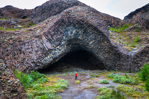 Woman admiring The Hljóðaklettar, cave formed with basaltic columns, twisted and angled in every conceivable direction. Formed for the Jökulsá River, the rocks at Hljóðaklettar have strange acoustical properties which reflect, enhance or mute the river’s roar, depending on where you’re standing. Hence the name “Echo Rocks”.