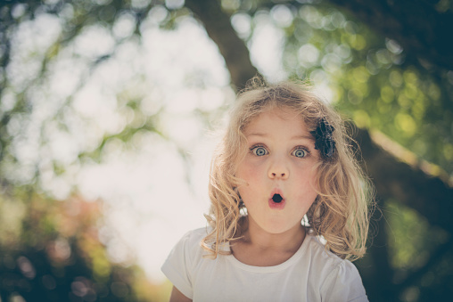 little surprised blond girl with blue eyes in a garden in summer