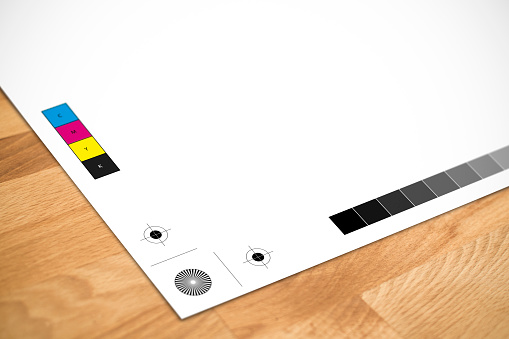 Piece of paper on a wooden surface with Printers Registration Marks and Colour Bars.