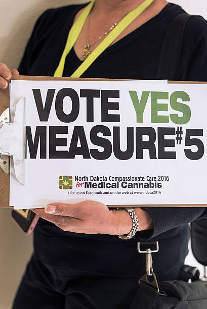 Activist for medical marijuana holding political sign Moorhead, Minnesota, United States - September 14, 2016: Political activist holding up clipboard urging people to vote for the North Dakota Compassionate Care Act in November, 2016. The act, known as Measure #5, would allow certain patients with dehabilitating conditions to obtain medical marijuana.  ballot measure stock pictures, royalty-free photos & images