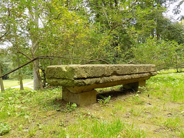 istock Old stone bench in park with many deciduous trees 610955572