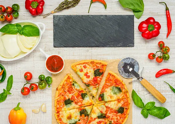 Italian Pizza sliced with Pizza-cutter Wheel and mozzarella cheese and Vegetables. Dark Stone Plate as Copy Space Area