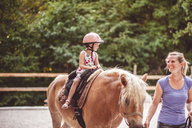 little girl taking horse-riding lessons - teaching child horseback riding horse imagens e fotografias de stock