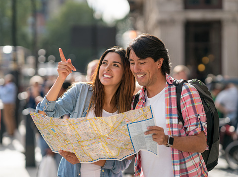 Happy couple sightseeing and holding a map looking for directions