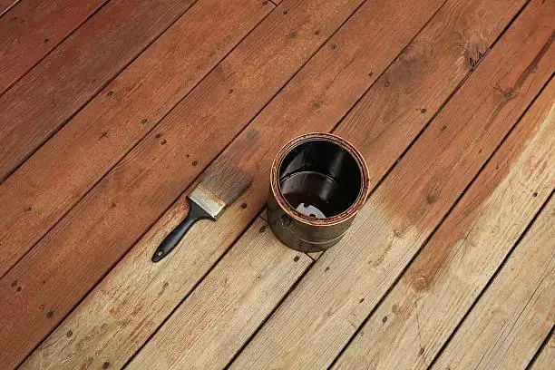 Photo of Partially stained deck; paint brush and a can of stain
