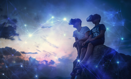 Father and son using Virtual Reality glasses sitting outside and watching futuristic network. Stock Photo. Creative Content Brief 603438805