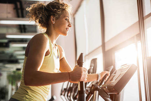 profil de jeune femme souriante faisant de l "exercice dans notre club de remise en forme. - cross trainer photos et images de collection