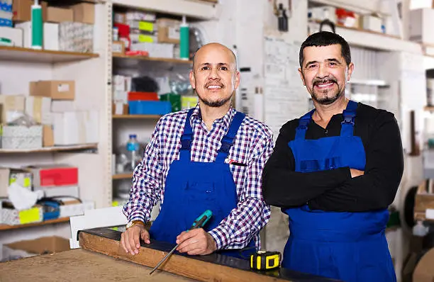 Photo of Two male woodworkers posing at workplace in workshop and smiling