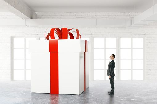 Businessman looking at huge present box in white brick interior. 3D Rendering