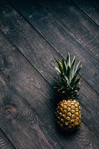 Single baby pine apple on a dark and grunge wooden background with copy space area