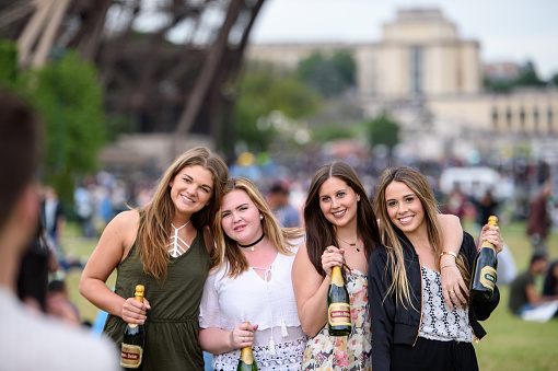 Paris, France - May 21, 2016: Four best friends posing with champagne bottle in the Champ De Mars, in front of Eiffel Tower during best travel to Paris, France