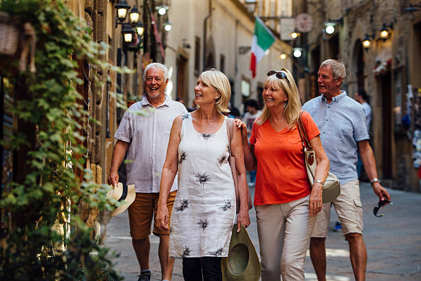 Mature Couples Looking Around Old Town Italy Mature couples looking around old town Italy as evening draws in. They walk down a narrow street while on holiday. Little lights can be seen outside of the buildings tourist couple candid travel stock pictures, royalty-free photos & images
