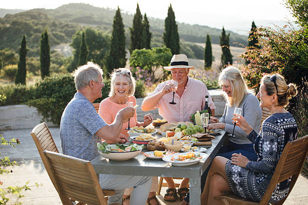 Great times with great friends A group of mature friends are sitting around an outdoor dining table, eating and drinking. They are celebrating their holiday with a glass of champagne and enjoying each others company. The image has been taken in Tuscany, Italy. old rich white guy stock pictures, royalty-free photos & images