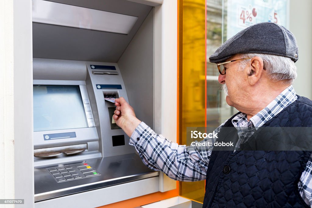 elderly man inserting credit card to ATM elderly man inserting credit card to ATM outdoor Senior Adult Stock Photo