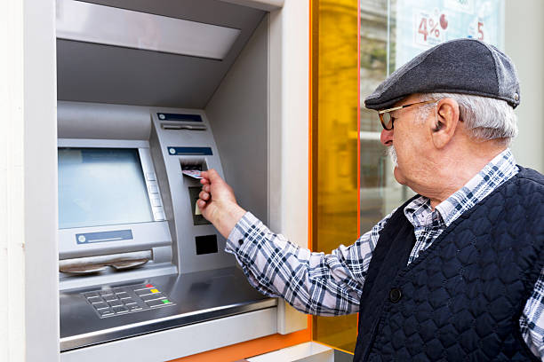 elderly man inserting credit card to atm - atm imagens e fotografias de stock