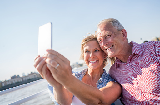 Happy adult couple in London sightseeing and taking a selfie on a boat