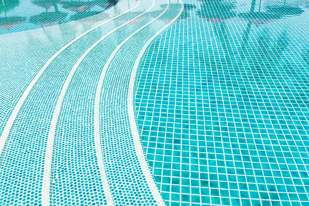Blue mosaic tile steps in empty green swimming pool.
