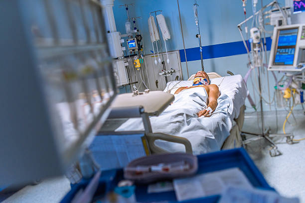 Young man lying in a hospital bed strapped to machines Young man in the intensive care unit lying in a bed strapped to medical equipment, which is all around him. intensive care unit stock pictures, royalty-free photos & images