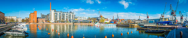Helsinki, Finland - May 17, 2015: Big blue panoramic skies over the cargo cranes, shipyards and working docks reflecting in the tranquil waters of Helsinki harbour overlooked by the modern waterfront developments of Finland's vibrant capital city.  Composite panoramic image created from twelve contemporaneous sequential photographs.