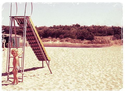 Vintage photo from the seventies of a little kid playing in a playground at the beach.