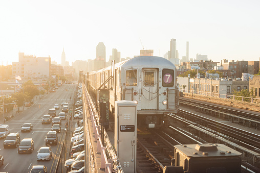 This is a color, horizontal photograph shot in the late afternoon during rush hour. both the public transit subway train and cars drive towards Sunnyside Queens from Manhattan as the sun is beginning to set. Photographed with a Nikon D800 DSLR camera in autumn.